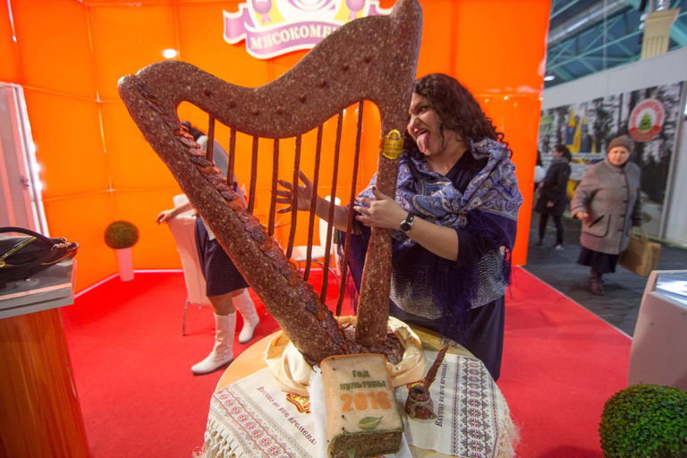 Женщина позирует для фотографии имитируя игру на арфе сделанной из колбасного мяса перед книгой из сала с надписью «Год культуры-2016»